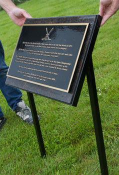 Framed metal stand holding brown granite backing board with bronze plaque attached.