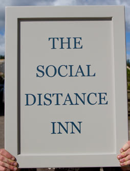 The social distance inn - a framed and painted wooden sign.